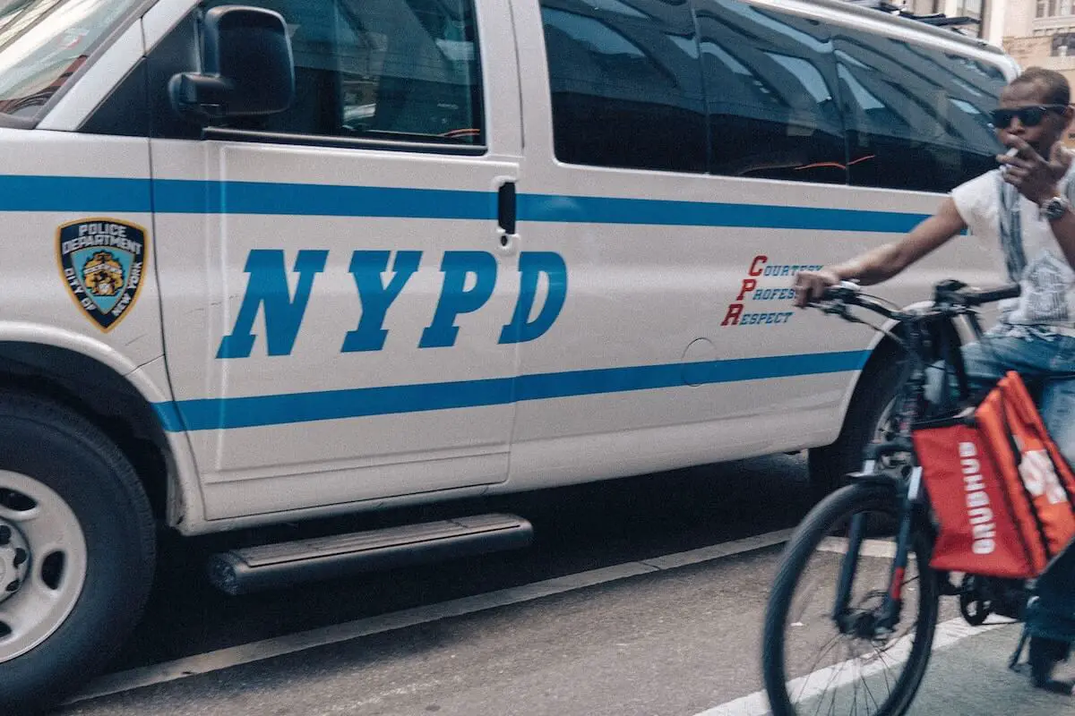 Food delivery cyclist breaking nyc bike laws next to police van.