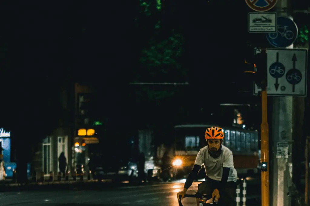Image of a cyclist wearing white t shirt and an orange helmet cycling at night. Source: Unsplash