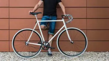 Image of a man wearing jean shorts holding a white fixed gear bike.