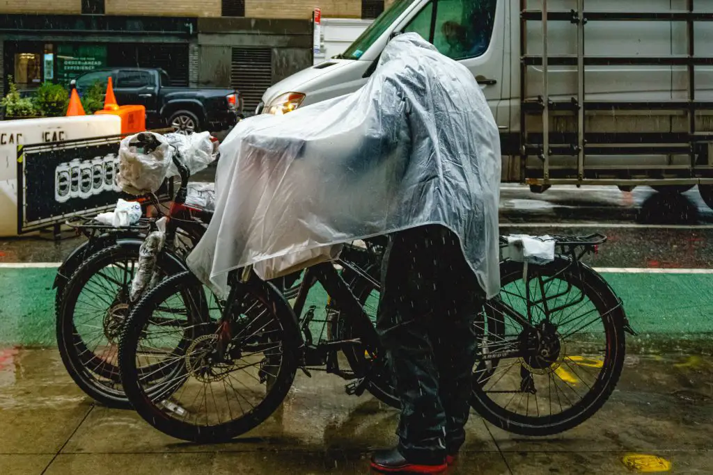Man wearing a raincoat standing beside his bike in the rain. Source: Unsplash