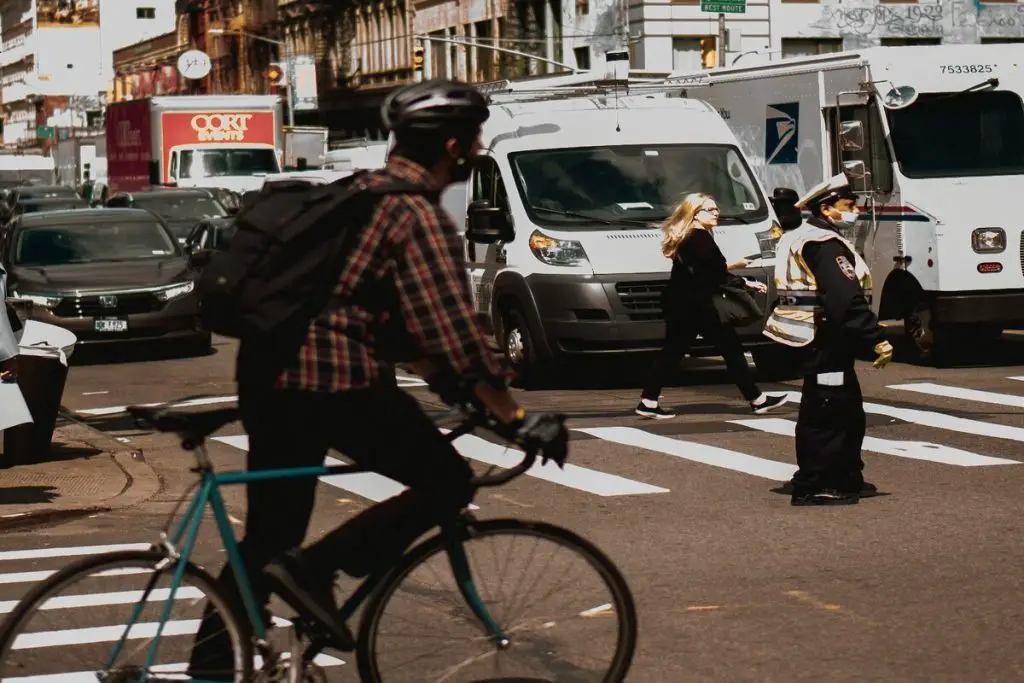 Image of a cyclist on a pedestrian lane and a woman crossing the street. Source: Unsplash