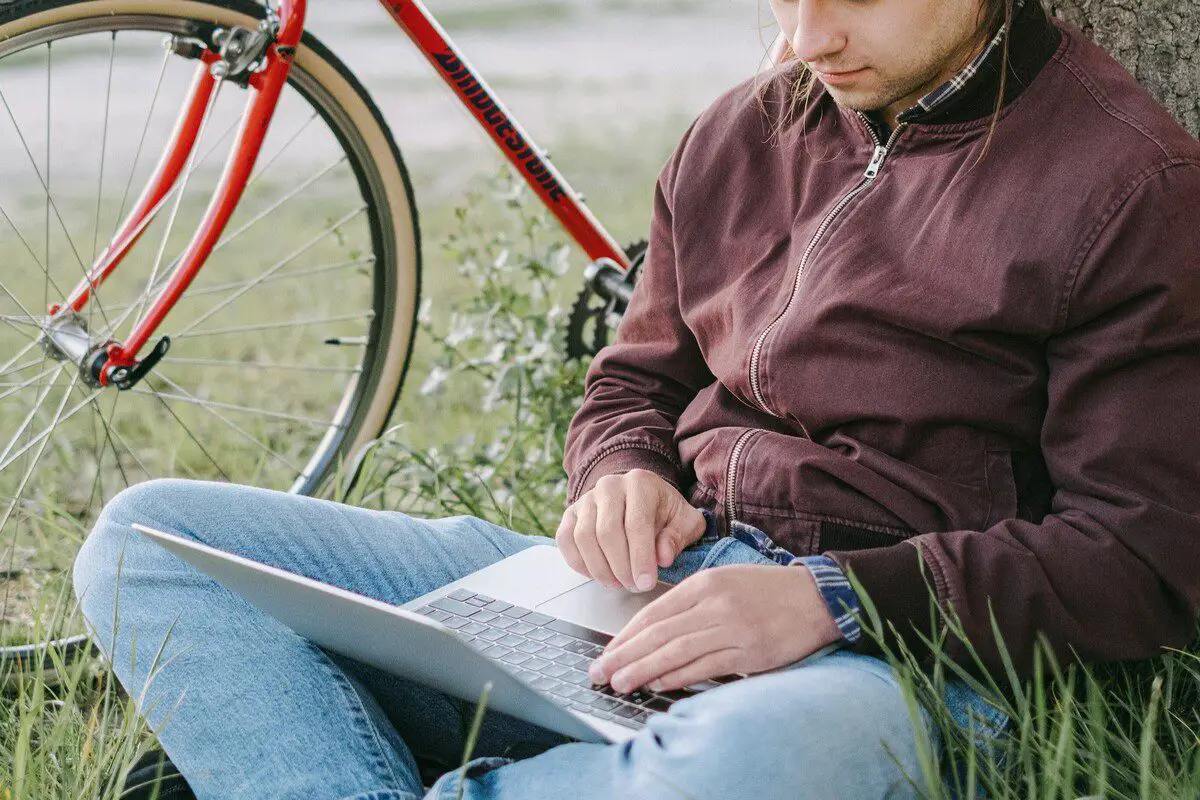 Image of a man using a laptop beside a bicycle. Source: pexels