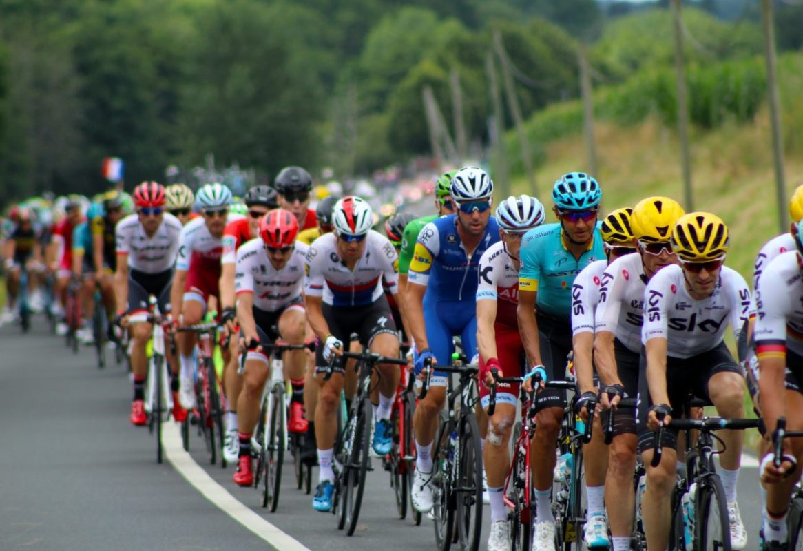 Image of cyclists racing wearing different colored helmets. Source: unsplash