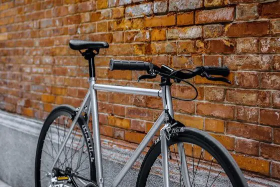 Gray fixed gear bike with thick-slick tires against brick background.