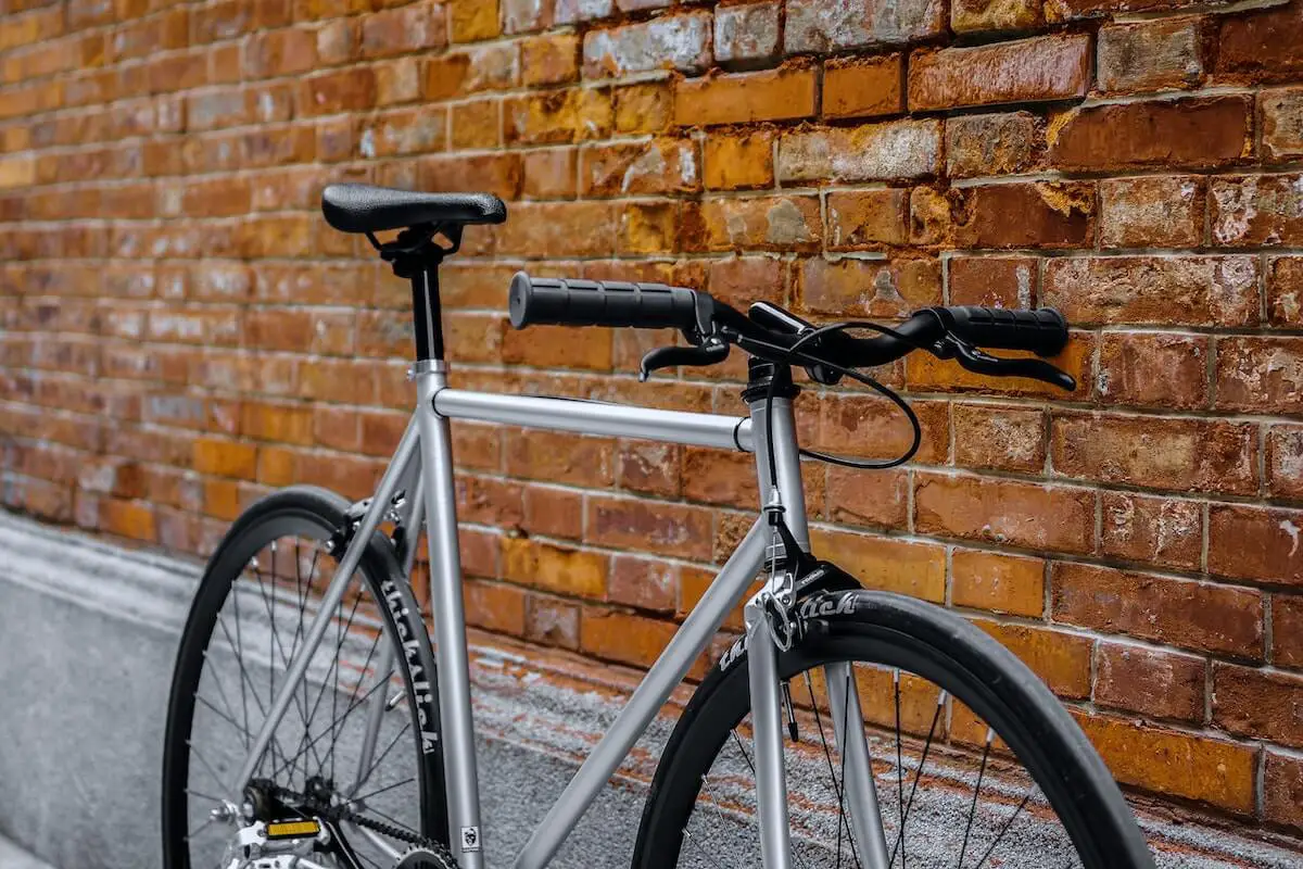 Gray fixed gear bike with thick-slick tires against brick background. Source: zifeng zhang, unsplash