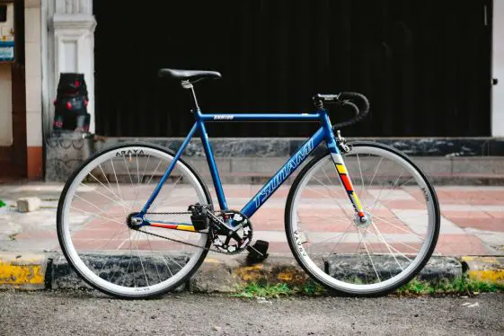 Blue tsunami snm100 single speed bike with drop bars and pedal straps on city streets.