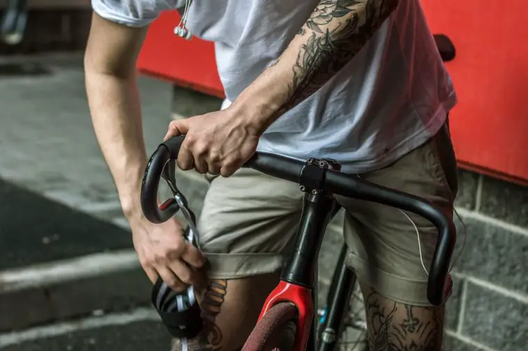 Fixed Gear Cyclist With Tattoos White Shirt And Headphones Riding A Black And Red Fixed Gear Bike Without Brakes - Why Fixed Gear Bikes Don't Have Brakes