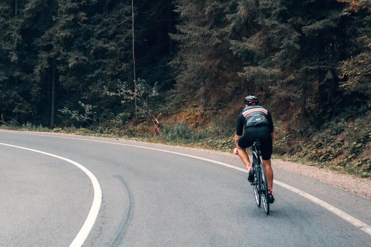 Image of a road cyclist climbing a hill near the forest. Source: viktor bystrov, unsplash