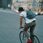Image of man riding fixie bicycle with blue backpack in the city streets. Source: Adobe Stock