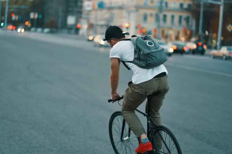 Image of man riding fixie bicycle with blue backpack in the city streets. Source: Adobe Stock