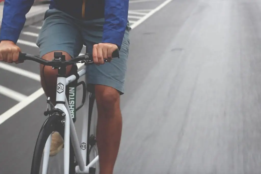 Man with blue jacket and shorts riding a white fixed gear bike