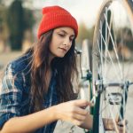 Young woman with orange cap replacing components on her fixed gear bike. Source: Adobe Stock