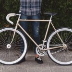 A man standing behind golden fixed gear bicycle. Source: Adobe Stock