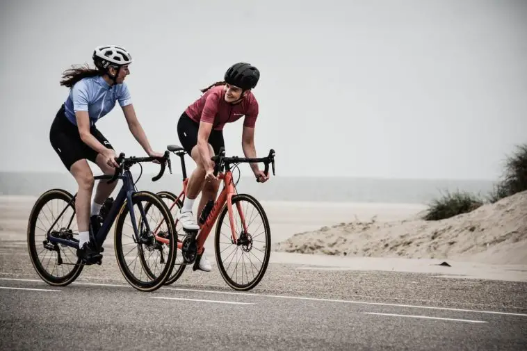 Image of two women cycling on road bikes by the beach. Source: Coen van de Broek, Unsplash