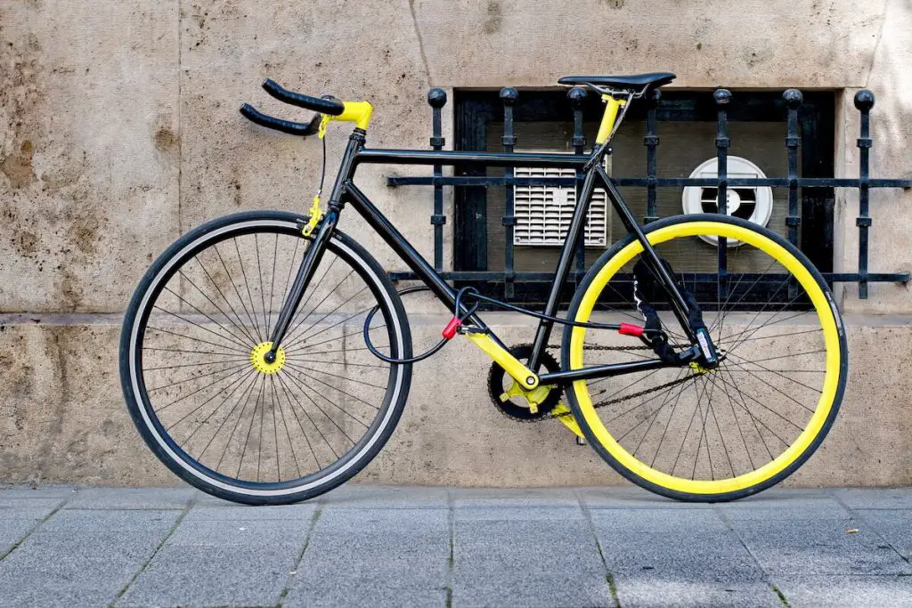 Black and yellow fixed gear bike locked properly with two chain locks. Source: adobe stock