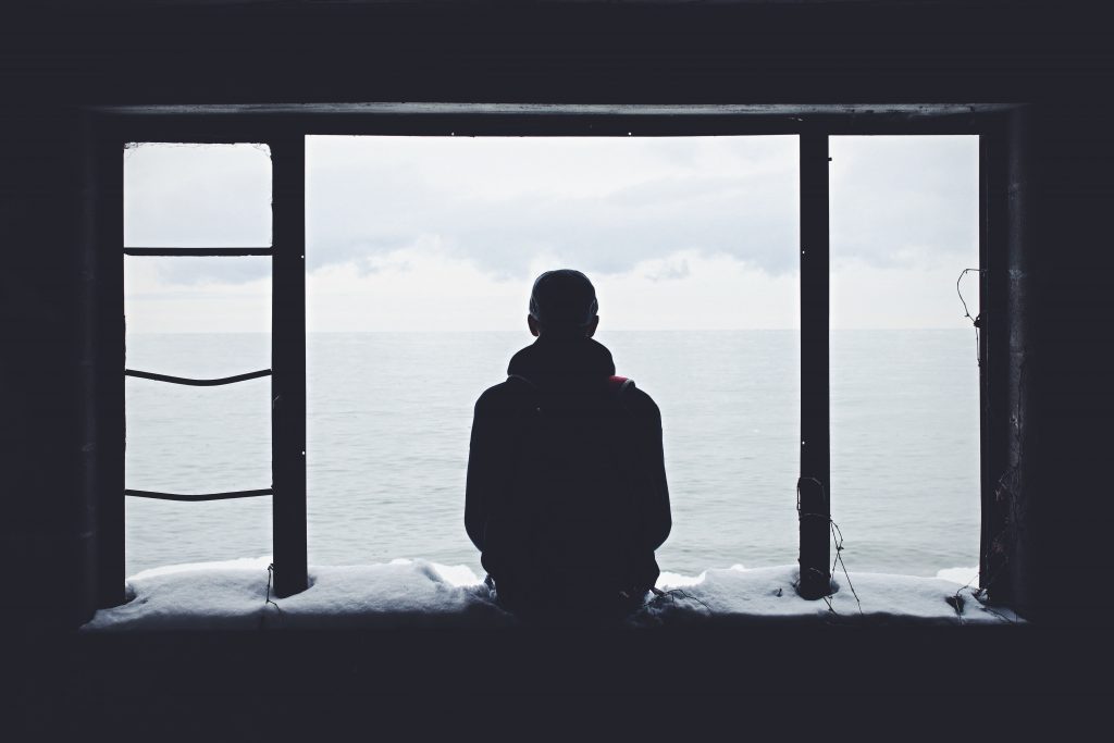 Image of a person sitting outside of a window staring at the ocean source. Source: noah silliman, unsplash