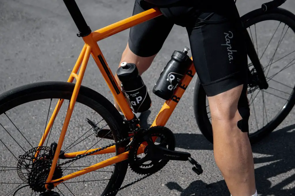 Image of a man in black cyclist shorts standing on an orange bike. Source: david dvoracek, unsplash