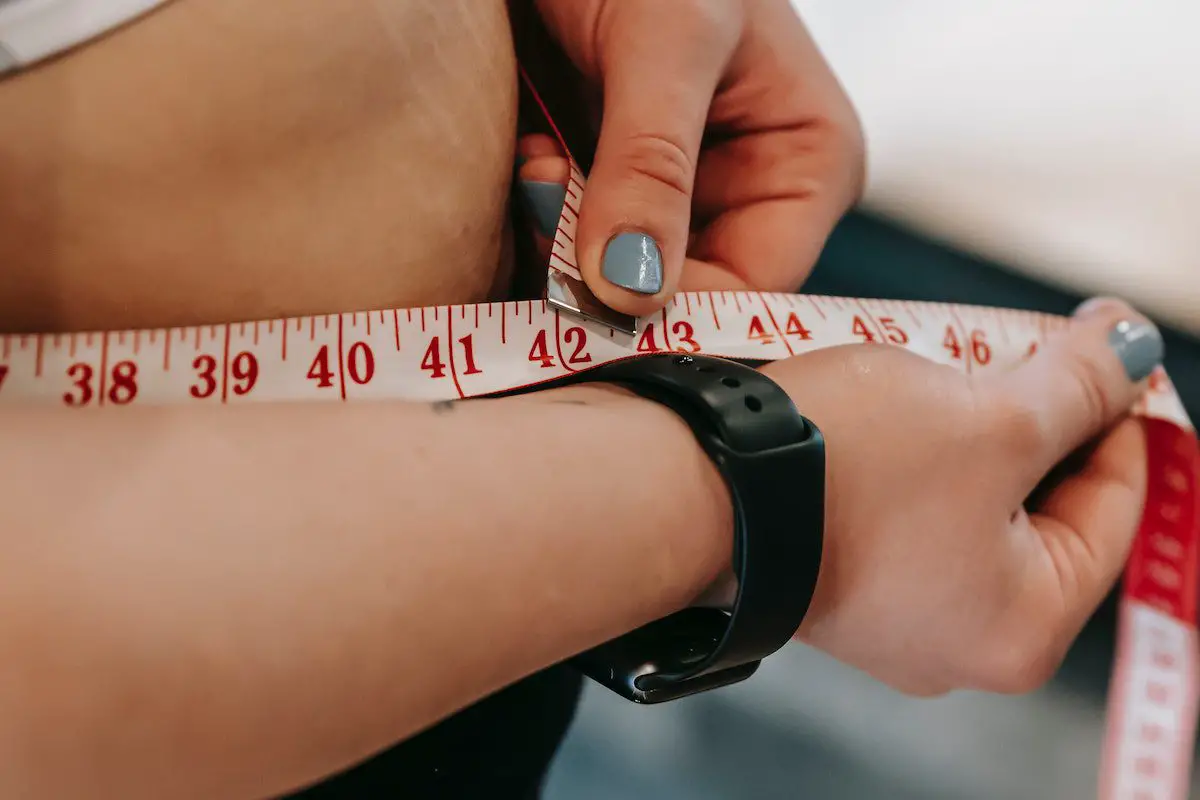 Image of a woman holding a tape measure to her belly. Source: andres ayrton, pexels