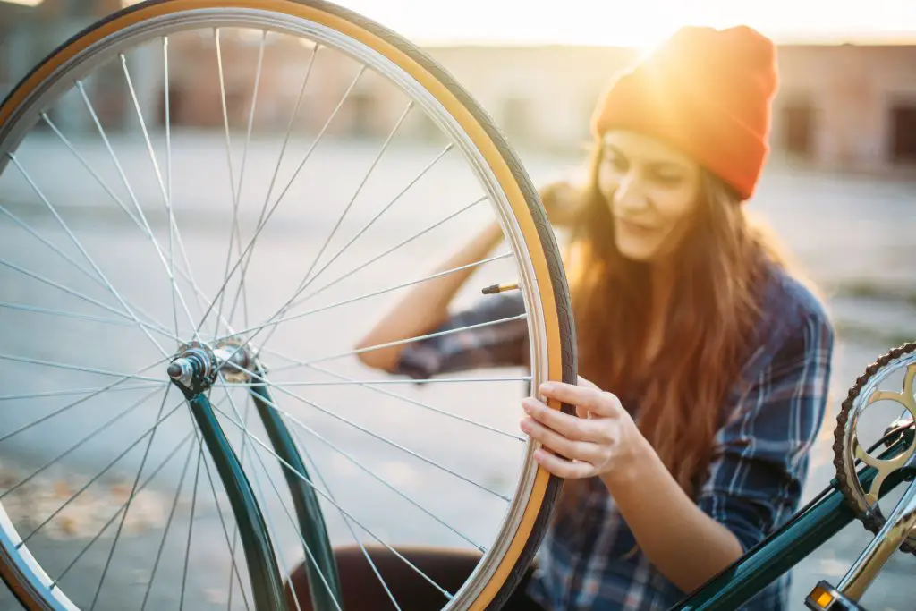Image of a female cyclist wearing an orange hat repairing a fixed gear bike wheelset. Source: adobe stock