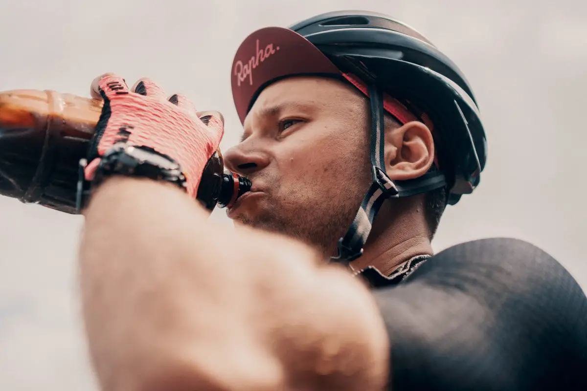 Image of a male cyclist wearing a helmet drinking from a bottle. Viktor bystrov, unsplash
