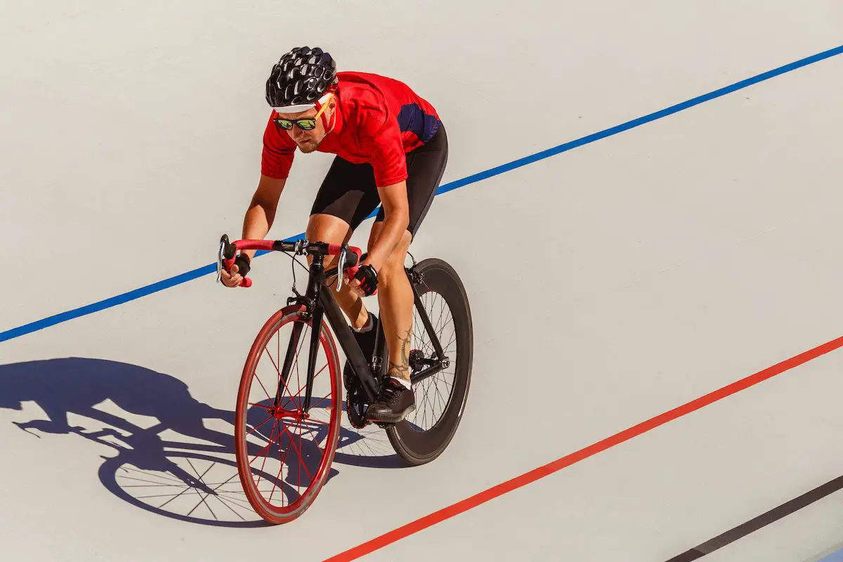 Image of a man on velodrome track wearing red jersey riding a track bike. Source: adobe stock