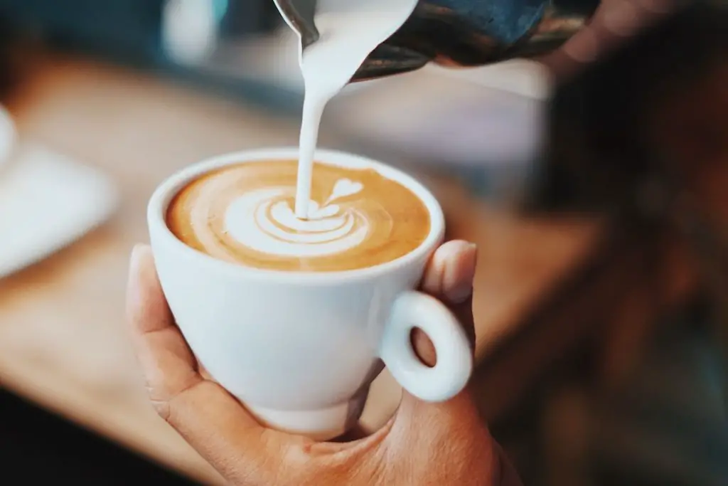 Image of cappuccino with frothed milk being poured over it. Source: unsplash