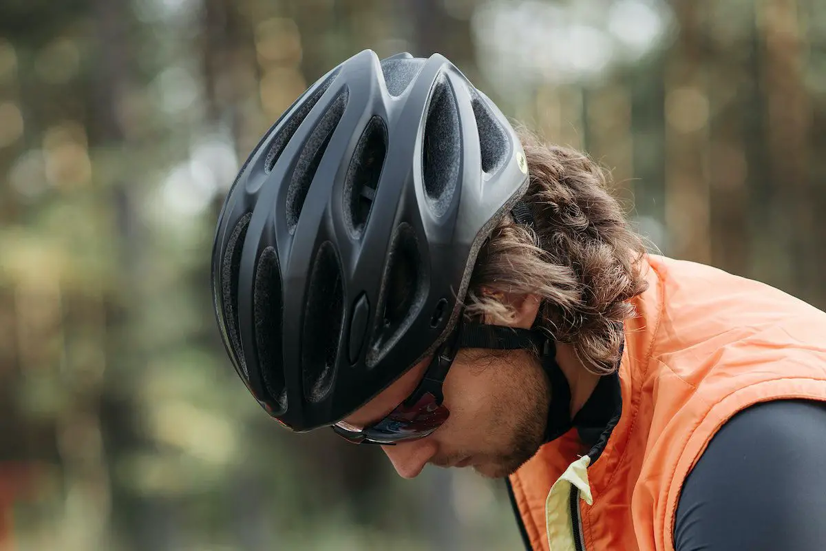 Image of cyclist wearing a orange vest and black helmet. Source: pavel danilyuk pexels