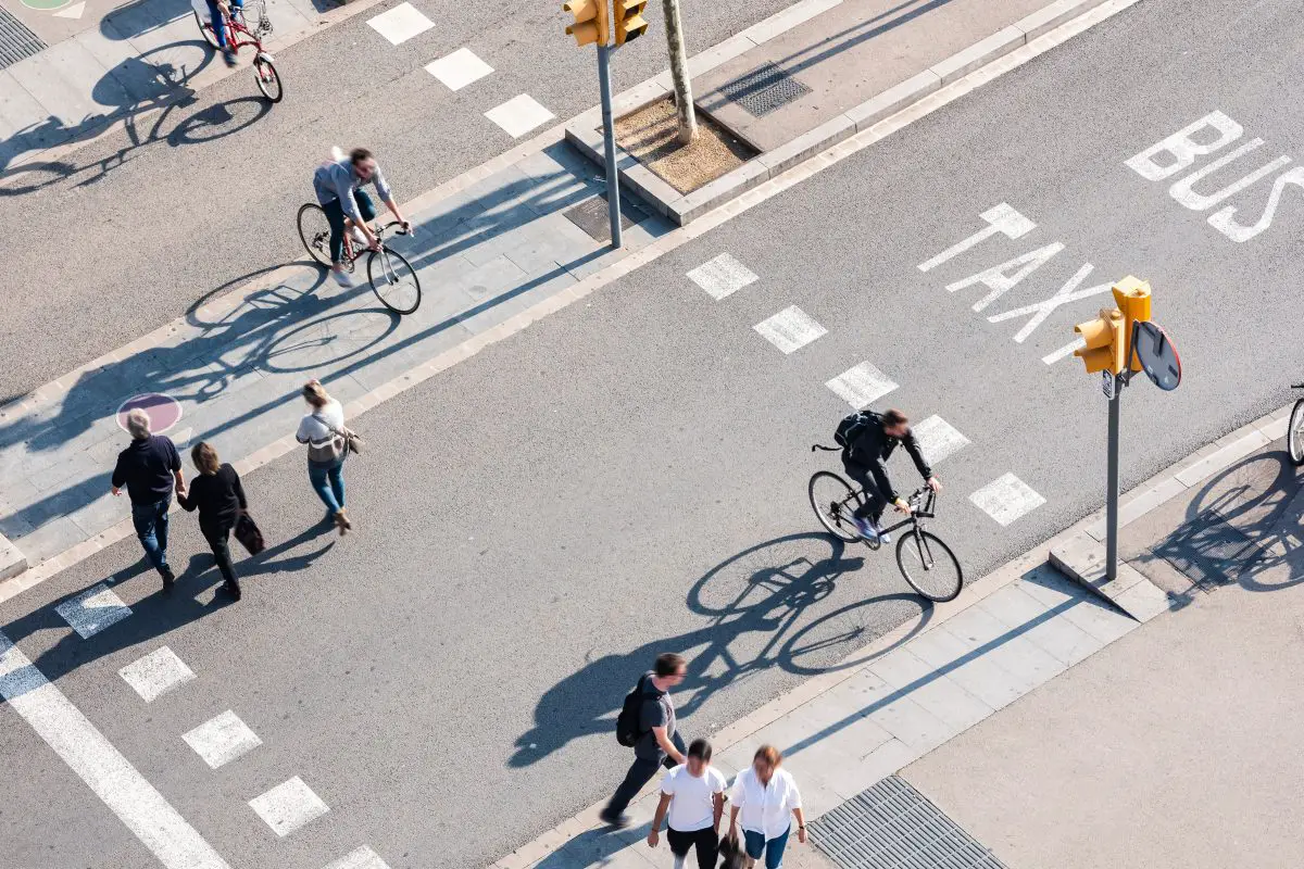 Image of people crossing street with a bike lane in a busy city. Source: adobe stock