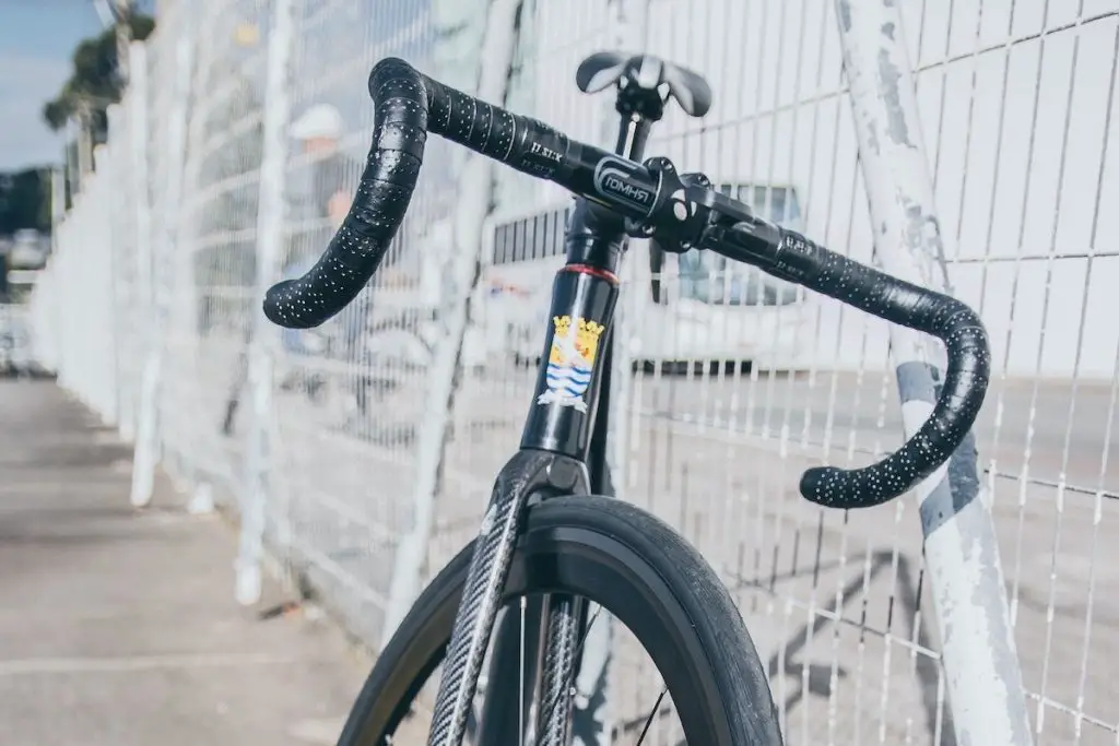 Image of a black fixed gear bike with drop bars leaning on an outdoor fence. Source: yuri catalano, unsplash