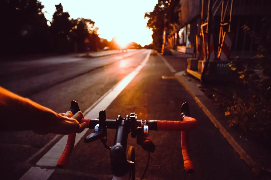 Mage of a cyclist holding the handlebars while riding a bicycle on the road. Source unsplash