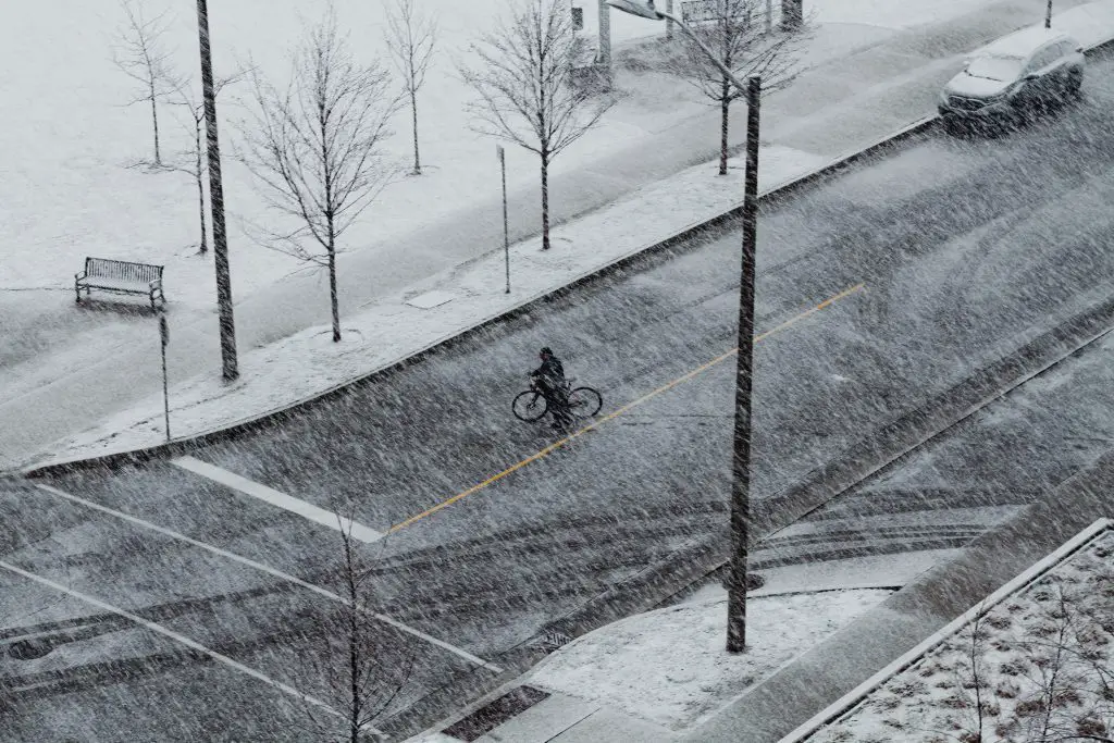 Cyclist riding a bike on the street in a snowstorm. Source: pexels