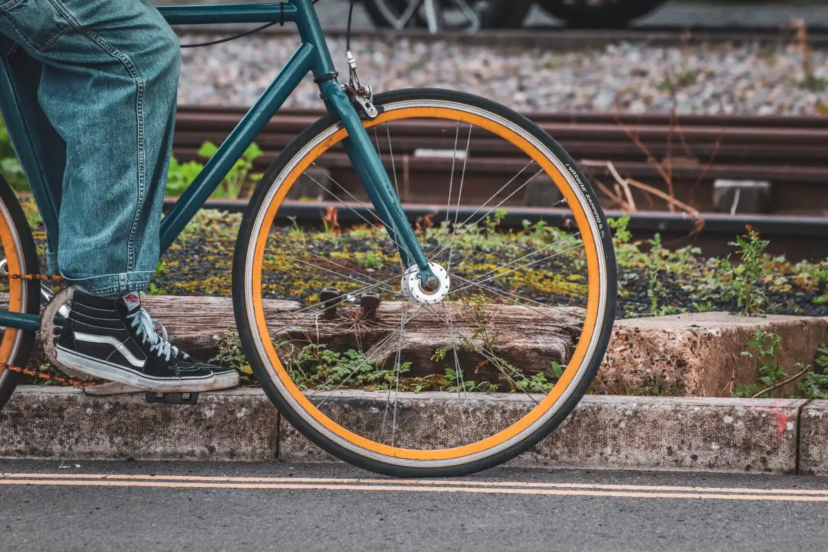 Closeup of a bicycle wheel with a person riding on the bicycle. Source: pexels