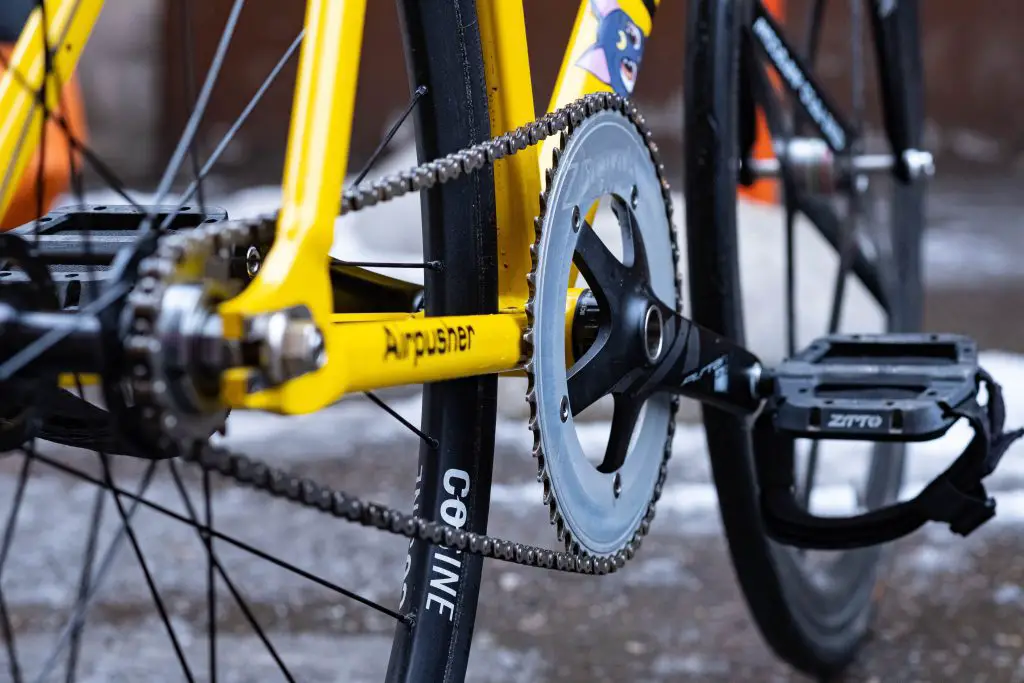 Closeup of a yellow bicycle wheel and pedal. Source: unsplash